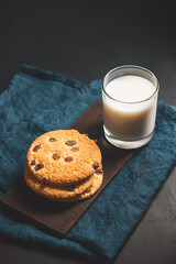 Crispy oatmeal cookies with raisins and glass with milk on wooden board, dark background
