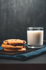 Crispy oatmeal cookies with raisins and glass with milk on wooden board, dark background