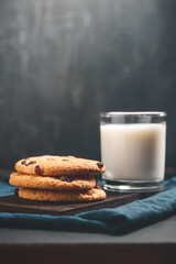 Crispy oatmeal cookies with raisins and glass with milk on wooden board, dark background