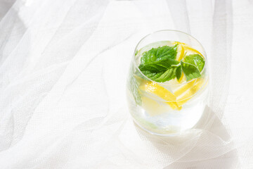 Close-up of homemade lemonade with lemon, mint and ice cubes in a glass on white wood table with white tulle fabric