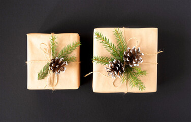 Two gifts in craft paper with a spruce branch and cones on a black background top view