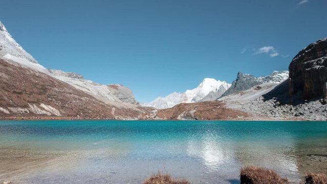 Milk lake with limestone mountain range and tourists travelling on Tibetan plateau in sunny day at Yading nature reserve