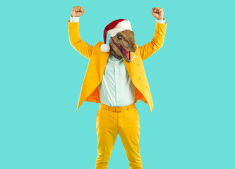 Fototapeta na wymiar Funny winner man wearing yellow suit, dinosaur mask and Christmas cap standing isolated on turquoise background, celebrating his victory in festive contest or competition event, and raising fists up