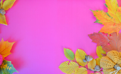 colorful autumn leaves with handmade crochet pumpkins on pink ground with space for text