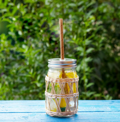 Natural lemonade in a glass jar with paper drinking straw on blue wooden table