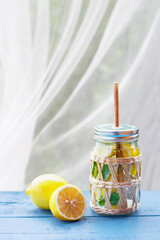 Natural lemonade in a glass jar with paper drinking straw on blue wooden table with lemons