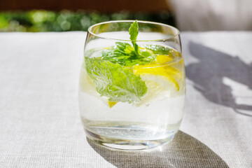 Close-up of homemade lemonade with lemon, mint and ice cubes in glass on a grey table