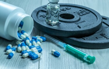 Closeup of illegal doping injectable drug and capsules and weight plates - cheating drug in sports