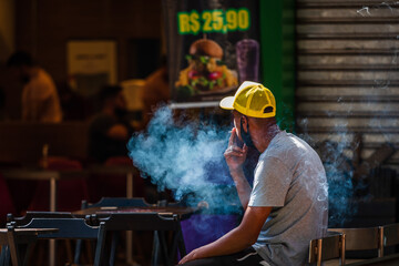 Young black Brazilian man smoking a cigarette outside of a burger restaurant at Savassi, Belo...