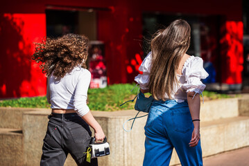 Two white Brazilian girls wearing white blouses and denim pants walking fast at Savassi, Belo Horizonte, Brazil.