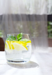 Close-up of homemade lemonade with lemon, mint and ice cubes in a glass on white wood table