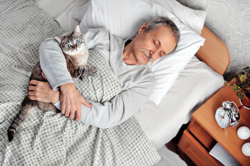 Sleeping senior man holding tabby cat on chest