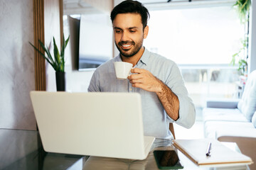 Man working at home using laptop drinking coffee