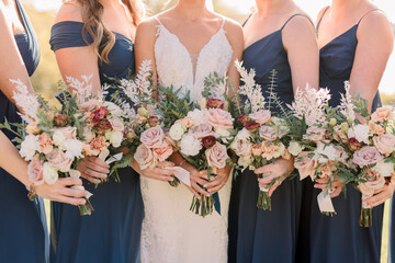 Bride and bridesmaids holding bouquets. Bridesmaids are wearing navy blue dresses. Bouquet has roses and wildflowers.  - obrazy, fototapety, plakaty
