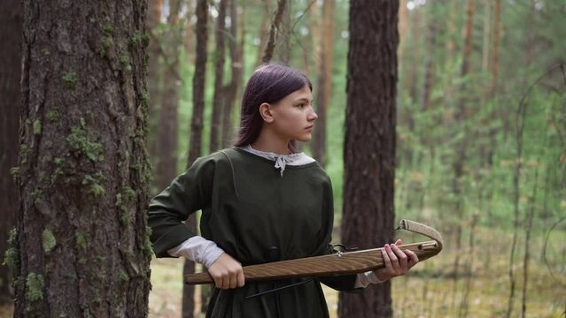 Careful girl with crossbow looks around walking through wood