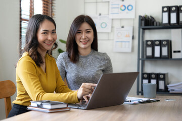 Two young Asian business woman talk, consult, discuss working with new startup project idea presentation analyze plan marketing and investment in the office.