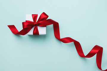Gift or present box with red bow ribbon on light blue background top view. Greeting card for...