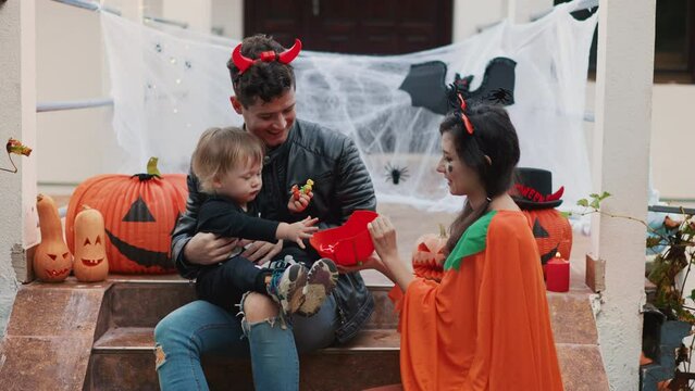 Happy multiethnic family - mother, father and little son celebrate Halloween at home at background of decorated with pumpkin lanern house. People have fun on traditional fall vibe. Love togetherness