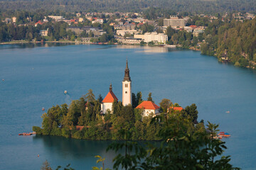 Church in the middle of lake bled in Slovenia at the golden hour with city in the background