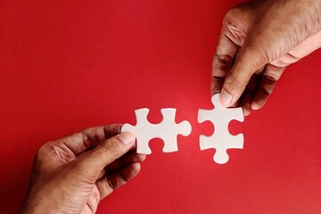 Two hands connect puzzle piece on red background. Teamwork, solutions, mergers and acquisitions...