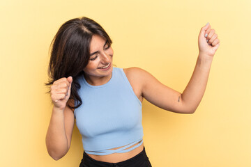 Young Indian woman isolated on yellow background dancing and having fun.