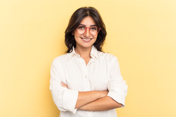 Young Indian woman isolated on yellow background who feels confident, crossing arms with determination.