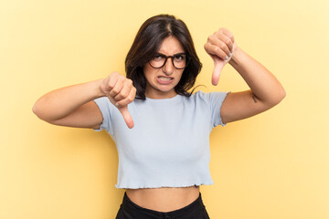 Young Indian woman isolated on yellow background showing thumb down and expressing dislike.