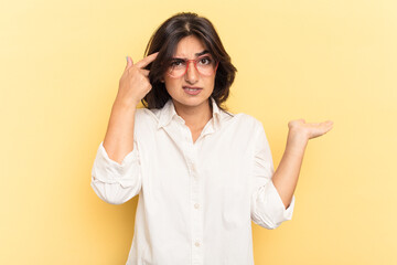 Young Indian woman isolated on yellow background holding and showing a product on hand.