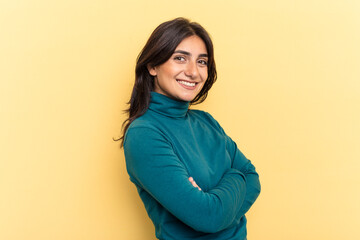Young Indian woman isolated on yellow background who feels confident, crossing arms with...
