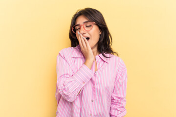 Young Indian woman isolated on yellow background yawning showing a tired gesture covering mouth with hand.