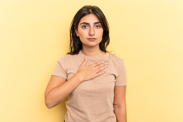 Obraz premium Young Indian woman isolated on yellow background taking an oath, putting hand on chest.