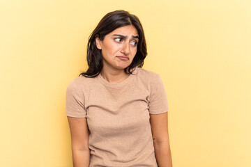 Obraz premium Young Indian woman isolated on yellow background shrugs shoulders and open eyes confused.