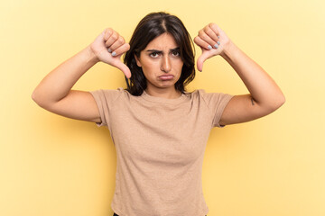 Young Indian woman isolated on yellow background showing a dislike gesture, thumbs down....