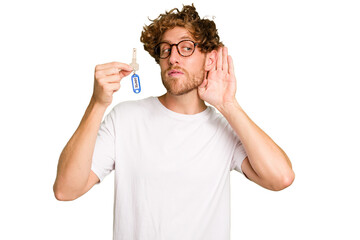 Fototapeta premium Young caucasian man holding home keys isolated on white background trying to listening a gossip.