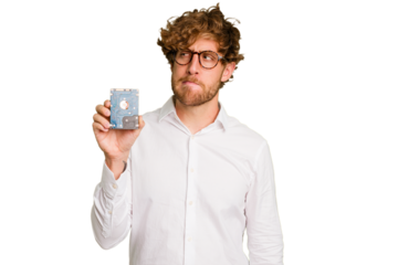 Young caucasian informatic man holding a hard drive isolated on white background confused, feels doubtful and unsure.