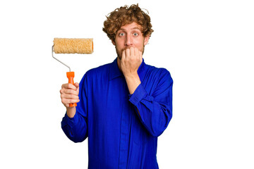 Young painter man holding a roll isolated on white background biting fingernails, nervous and very...