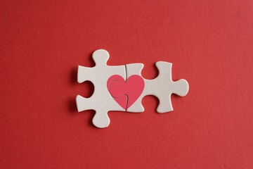 Top view image of connected jigsaw puzzle pieces with red heart icon on red background. Love and relationship concept
