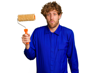 Young painter man holding a roll isolated on white background shrugs shoulders and open eyes confused.