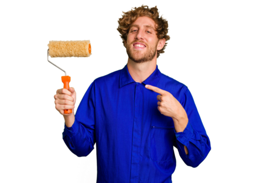 Young painter man holding a roll isolated on white background smiling and pointing aside, showing something at blank space.