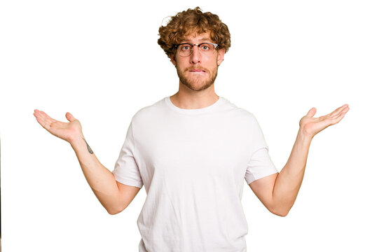 Young caucasian man isolated on green chroma background confused and doubtful shrugging shoulders to hold a copy space.