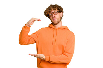 Young caucasian man isolated on green chroma background holding something with both hands, product presentation.