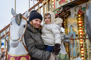 Fototapeta na wymiar Cheerful mother and baby girl riding on carousel horse during Christmas holidays
