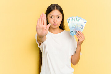 Young asian woman holding a banknotes isolated on yellow background standing with outstretched hand...