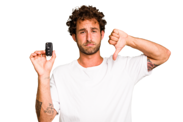 Young caucasian man holding car keys isolated showing a dislike gesture, thumbs down. Disagreement concept.