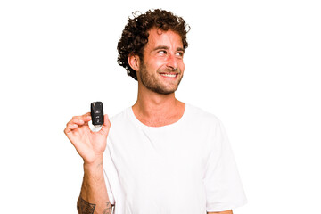 Young caucasian man holding car keys isolated looks aside smiling, cheerful and pleasant.