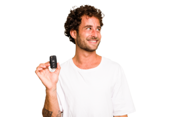 Young caucasian man holding car keys isolated looks aside smiling, cheerful and pleasant.