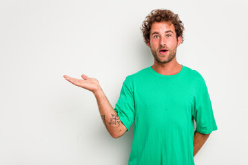 Fototapeta premium Young caucasian curly hair man isolated on white background impressed holding copy space on palm.