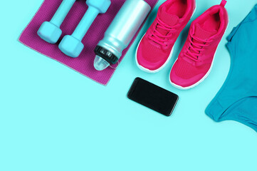 Smart phone and a set of fitness clothes on teal background top view