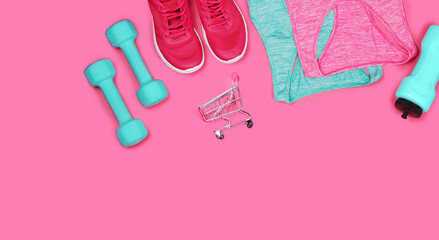 Top view still life of sneakers, dumbbells, water bottle and sportive tops on pink background