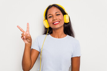 Young Indian woman listening to music wearing headphones isolated on white background joyful and carefree showing a peace symbol with fingers.